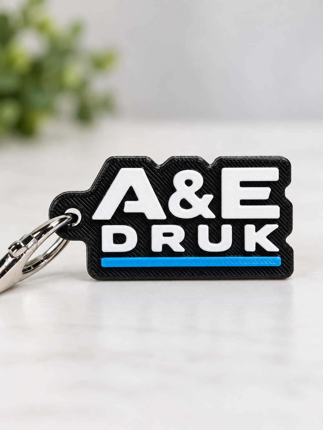 Brelok A&E Druk z wypukłymi białymi literami i niebieskim paskiem